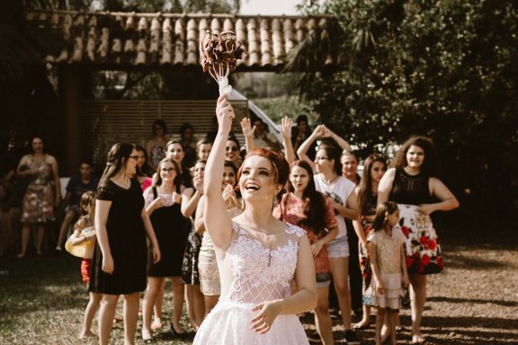Braut wirft ihren Strauß in die Luft, umgeben von jubelnden Frauen, die versuchen, ihn zu fangen, in einer festlichen Umgebung.
