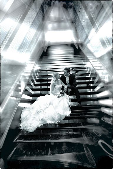 Braut und Bräutigam in einem stilisierten Schwarz-Weiß-Foto, das Zärtlichkeit auf einer modernen Treppe festhält.
