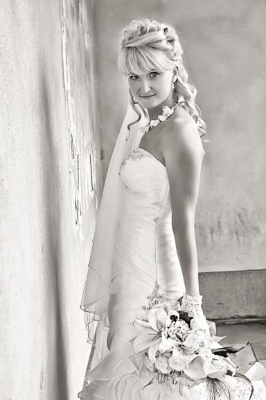 Braut schaut über ihre Schulter, trägt ein strapless Hochzeitskleid und hält einen Blumenstrauß in einer sanften Umgebung.
