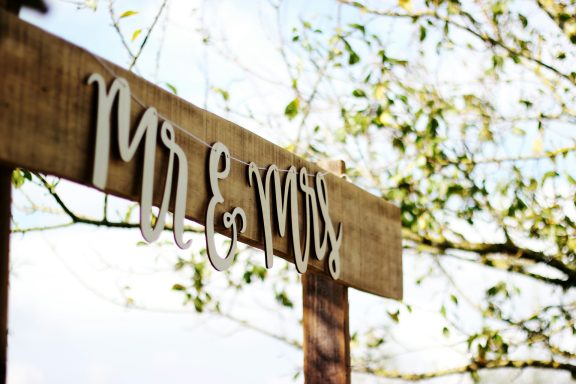 Holzschild mit "Mr. & Mrs." vor einer naturnahen Kulisse, ideal für Hochzeiten oder romantische Anlässe.
